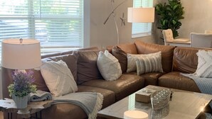 Ein Wohnzimmer mit einem braunen Ledersofa, weißen Kissen, einem Glastisch und einer Lampe.