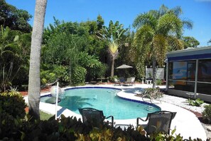 Una piscina circondata da vegetazione rigogliosa, con lettini e una zona relax coperta.