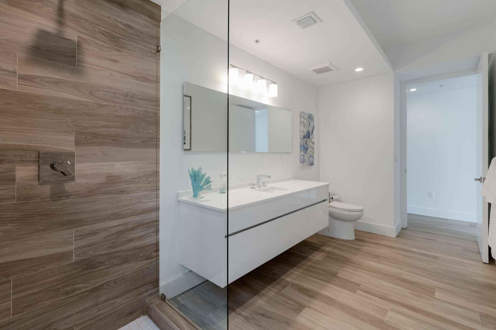 Un baño moderno con mampara de vidrio, lavamanos blanco y retrete.