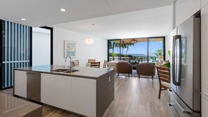 A modern kitchen with a central island, a dining area with chairs, and a large refrigerator. - NEW Luxurious Condo/inlet & Ocean Views 106 Inlet Way Unit 103 - Palm Beach Shores (Singer Island)