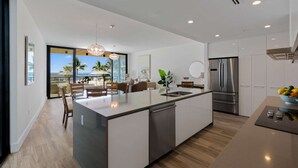 A modern kitchen with a central island, stainless steel appliances, and a view of the ocean. - NEW Luxurious Condo/inlet & Ocean Views 106 Inlet Way Unit 103 - Palm Beach Shores (Singer Island)