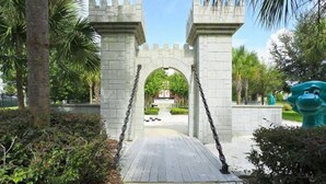 A stone archway with a pathway leading through it, surrounded by greenery and a statue. - Welcome to The Windsor Dream! (Kissimmee)
