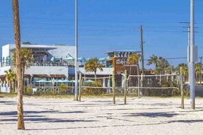Een strandvolleybalveld met een net, palmbomen en een gebouw met een bord waarop 