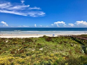 Een strand met een houten pier die naar het strand loopt, grasduinen en de oceaan.