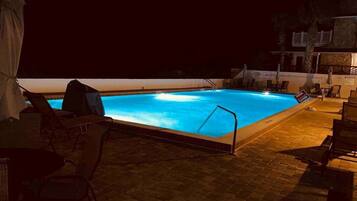 A nighttime swimming pool with a 'POOL CLOSED' sign, lounge chairs, and a covered seating area.