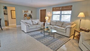 Ein Wohnzimmer mit zwei weißen Sofas, einem Glastisch und einem gemusterten Teppich.