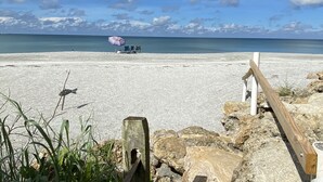 Ein Strand mit einer Holzzaun, einem gestreiften Sonnenschirm und Stühlen, die zum Meer hinweisen.