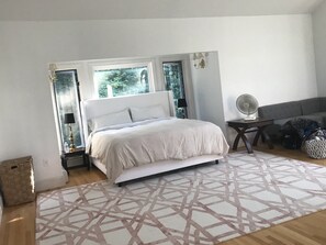 Relax in a spacious bedroom with a large bed, two windows offering a view of lush greenery, and a convenient desk area.