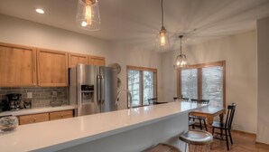 A modern kitchen with wooden cabinets, stainless steel appliances, a large island with stools, and pendant lighting.