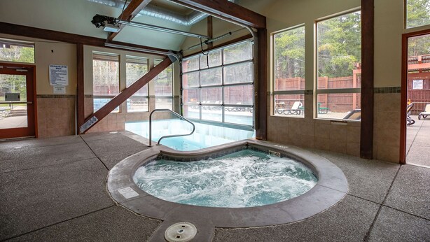 A hot tub area with a view of a pool and a wooden deck outside.