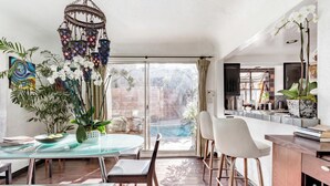 Una cocina moderna con una mesa de comedor de vidrio, taburetes de bar y vista a una piscina.