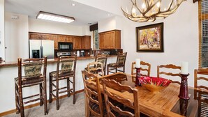 Ein Essbereich mit Holztisch und -stühlen, einer Chandelüster und einer Küche im Hintergrund.