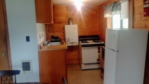 A compact kitchen with wooden walls, a stove, a refrigerator, and a sink.
