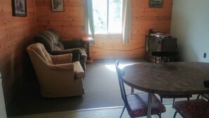 A cozy room with a sofa, armchairs, a dining table with chairs, a television, and a window with curtains.