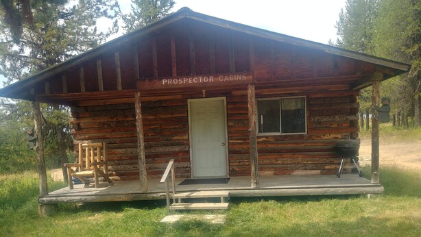 A rustic cabin labeled "Prospector Cabins" with a porch, a door, and a grill outside.