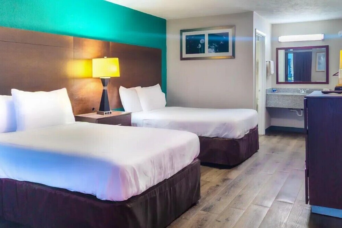 Une chambre d’hôtel avec deux lits, une table de chevet avec une lampe, une salle de bain avec un miroir et un bureau.