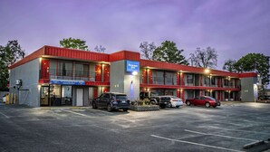 A motel with a red and grey exterior, multiple parking spaces, and a sign indicating the name and address. - Rodeway Inn (Augusta)