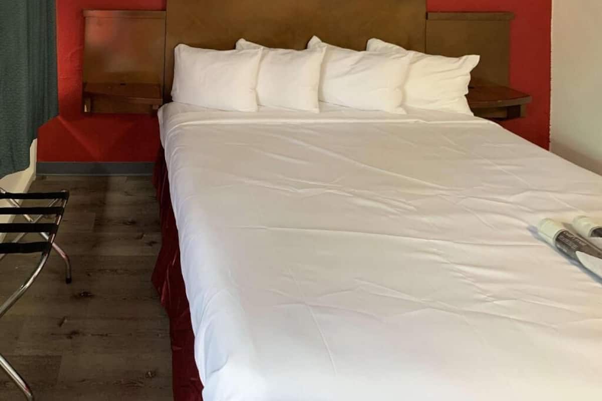Un lit bien fait, avec du linge de lit blanc, une tête de lit en bois et un mur rouge.