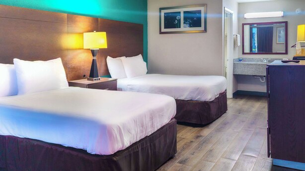 A hotel room with two beds, a nightstand with a lamp, a bathroom with a mirror, and a wooden floor. - Rodeway Inn (Augusta)