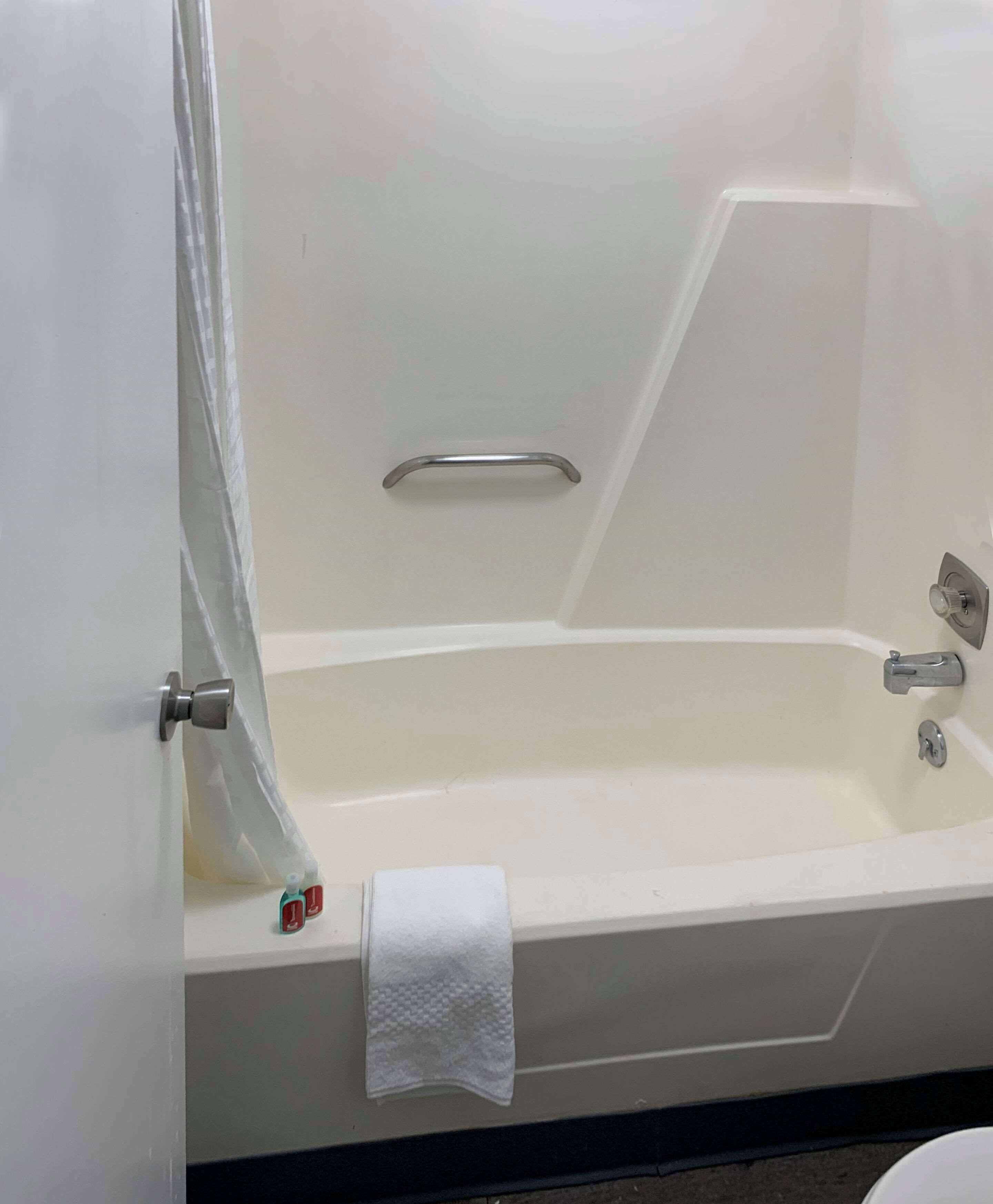 A white bathtub with a shower curtain, a towel, and a grab bar.