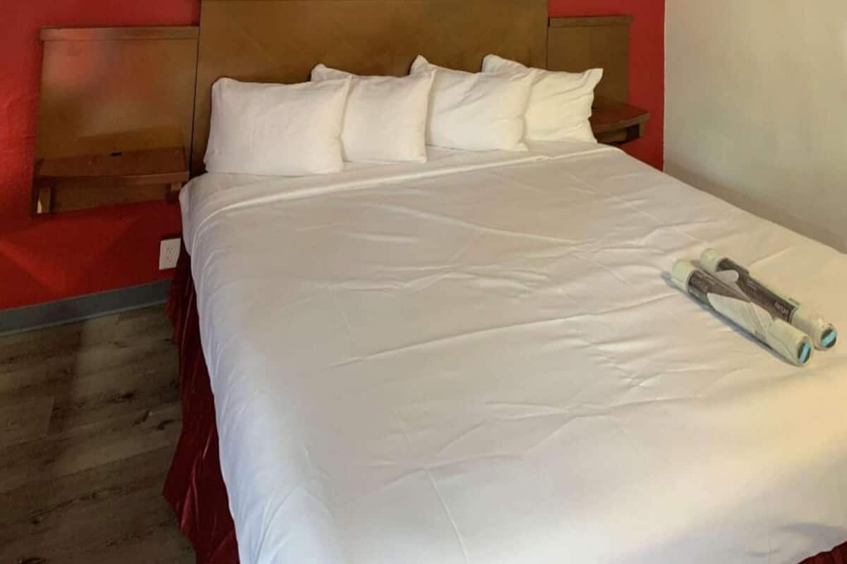 Un lit bien fait, avec du linge de lit blanc et des oreillers, une tête de lit en bois et une table de chevet en bois avec une lampe.