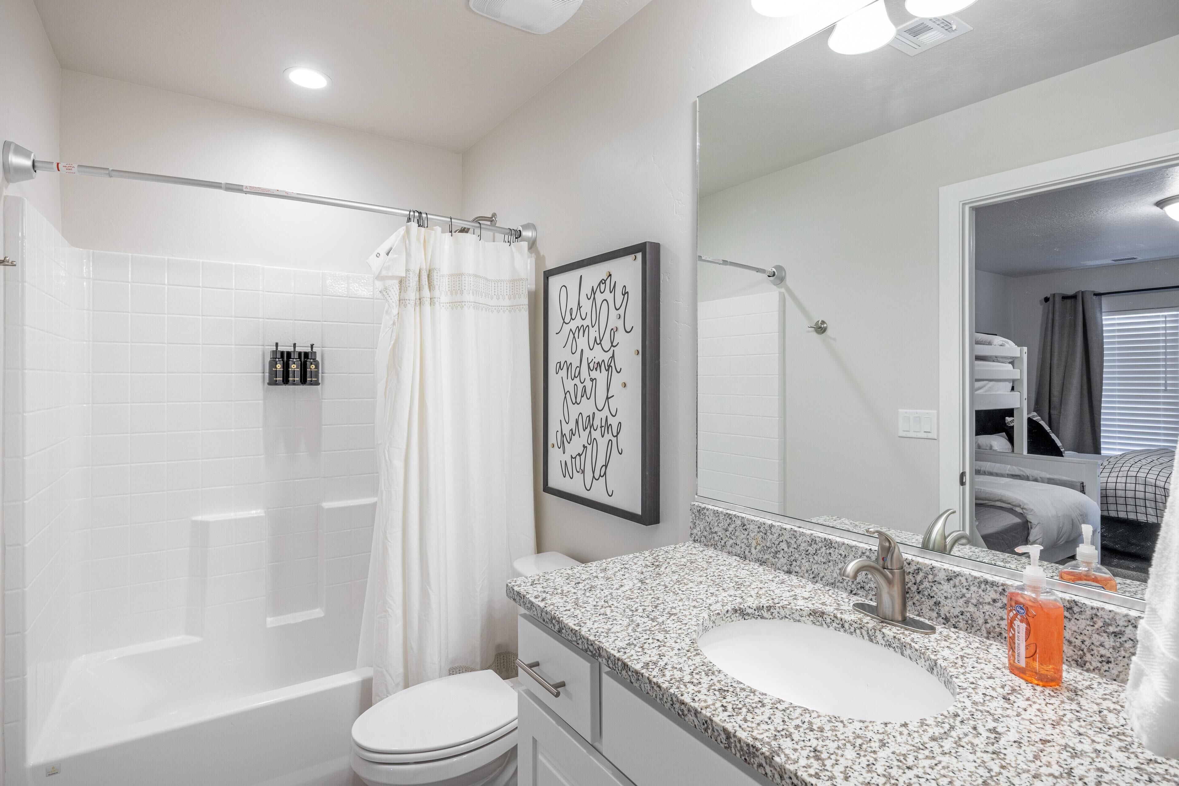 A bathroom with a bathtub, toilet, and sink. There is a shower curtain, a framed inspirational quote, and a mirror.