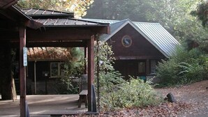 A rustic wooden pavilion with a metal roof, surrounded by dense foliage and a building labeled "Wildlife Cafe." - Zen themed private retreat in NW Portland. (Portland)