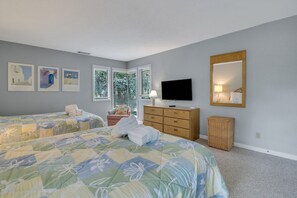 Une chambre avec deux lits, une télévision, une commode et une fenêtre avec des stores.