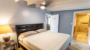 A bedroom with a bed, bedside table, and a lamp. There is a door leading to a bathroom. - PRIVATE Beachview Cottage Steps to Cane Bay Beach (St Croix)