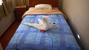 A bed with a blue and white patterned bedspread, a wooden headboard, a white pillow, and a roll of toilet paper on the side. - Hospedaje Ollantays (Cusco)