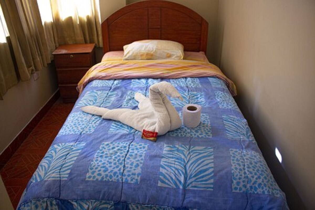 Un lit avec une couvre-lit à motifs bleus et blancs, une tête de lit en bois, un oreiller blanc et un rouleau de papier toilette posé sur le côté.