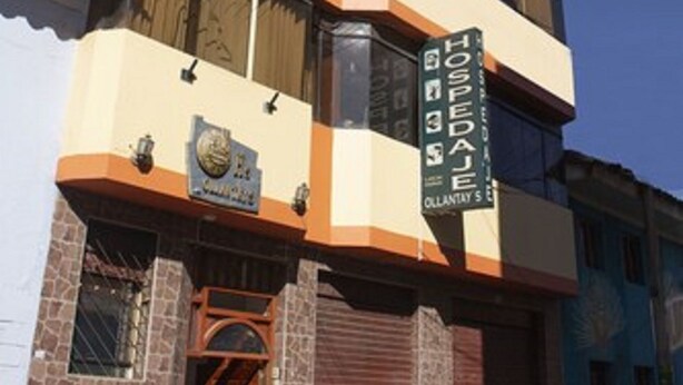 A multi-story building with a beige facade, a wooden door, and a sign that reads "HOSPEDAJES OLLANTAY AC". - Hospedaje Ollantays (Cusco)