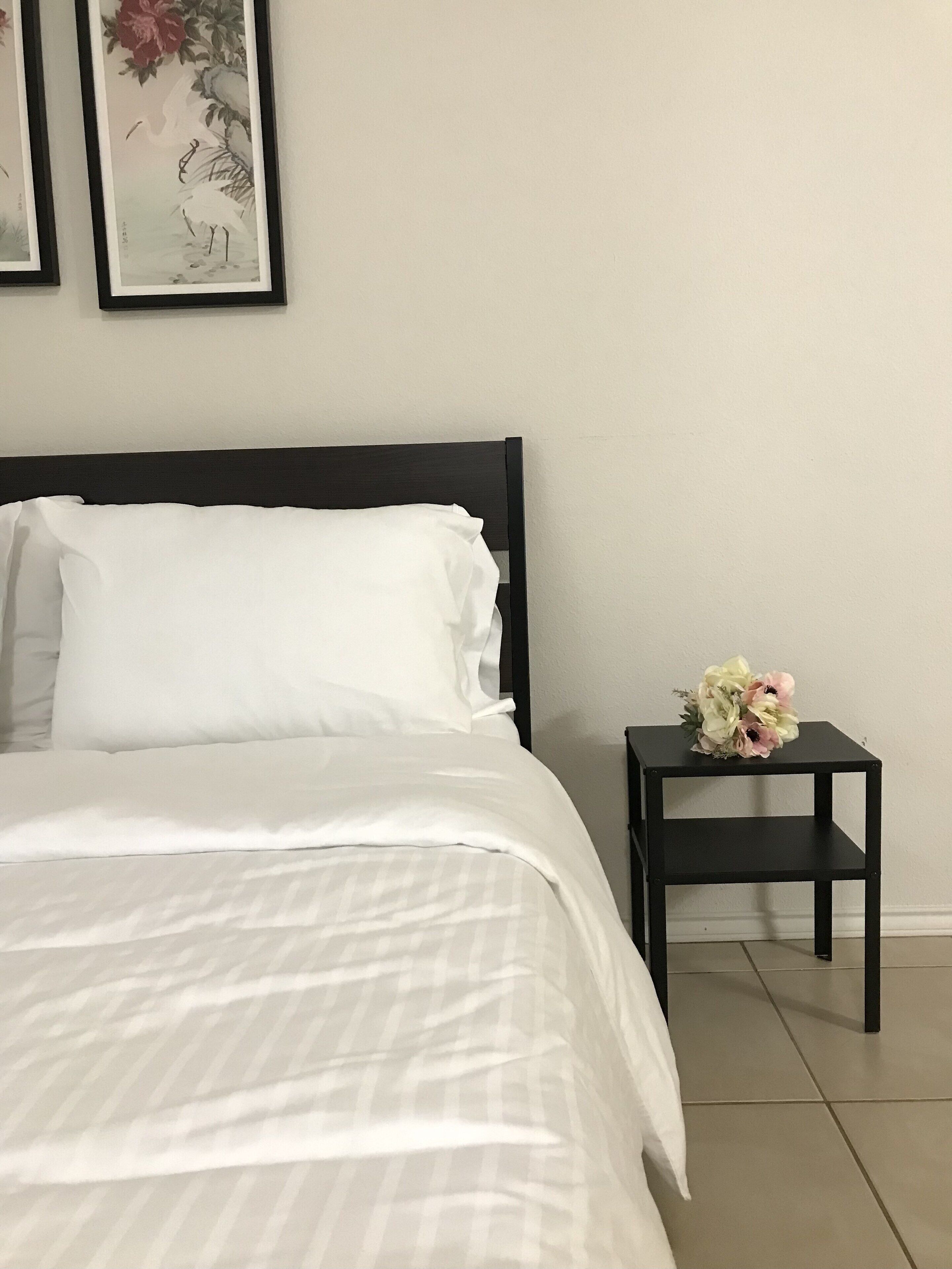Ein ordentlich bezogenes Bett mit weißen Leinen, einem schwarzen Kopfteil und einem kleinen Nachttisch mit Blumenstrauß.