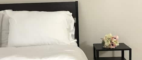 Un lit bien fait, avec du linge de lit blanc, une tête de lit noire et une petite table de chevet noire sur laquelle est posé un bouquet de fleurs.