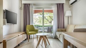 A modern hotel room with a sofa, a small round table, a TV, and a balcony with curtains.