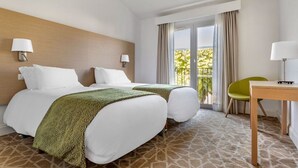 A hotel room with two beds, a balcony with curtains, a small table, and a chair.