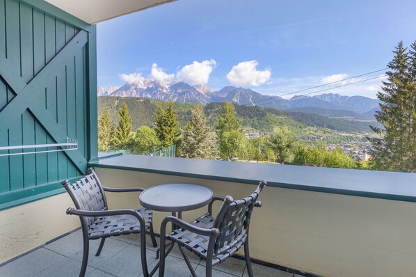A balcony with two chairs and a table, offering a view of mountains and a town.