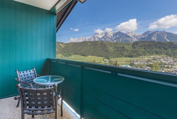 A balcony with a view of mountains, a table, and two chairs.