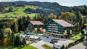 A hotel with a central building and a parking area, surrounded by trees and hills.