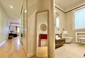 Une chambre d’hôtel moderne avec un plancher en bois, un grand miroir, une armoire rouge, des toilettes blanches et une fenêtre donnant sur un beau paysage.