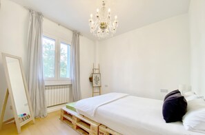 Une chambre à coucher avec un lit, un lustre, une fenêtre avec des rideaux, un radiateur et une échelle.