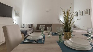 A dining area with a table set for four, a sofa, a bed, and a television mounted on the wall. - GuestHost - Elegant and modern 60sqm apartment that can accommodate up to 4 people. Located on the third floor, with elevator (not suitable for disabled people), of a characteristic building in San Lorenzo area, the apartment is about 15 minutes walk fro (Roma)