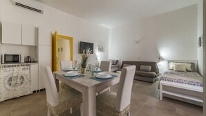 A modern, well-lit room with a dining table set for two, a sofa, a bed, and a kitchen area with a microwave. - GuestHost - Elegant and modern 60sqm apartment that can accommodate up to 4 people. Located on the third floor, with elevator (not suitable for disabled people), of a characteristic building in San Lorenzo area, the apartment is about 15 minutes walk fro (Roma)