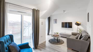 A modern living room with a blue sofa, a grey sofa, a flat-screen TV, and a large window with curtains.