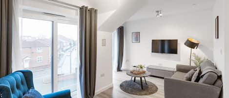 Una sala de estar moderna con un sofá azul, un sofá gris, un televisor de pantalla plana y un ventanal con cortinas.