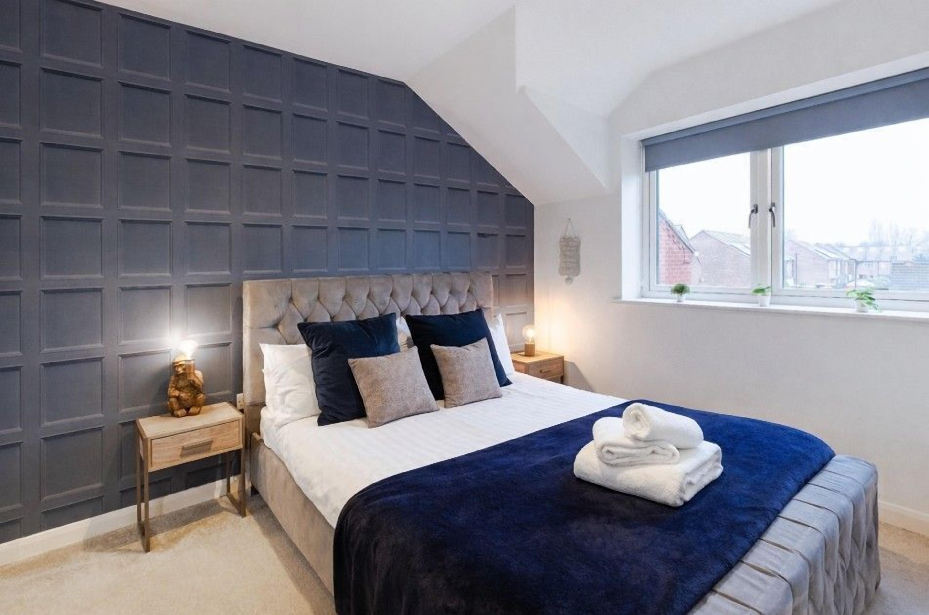 A bedroom with a tufted headboard, a large window, and a neatly made bed with a blue blanket.