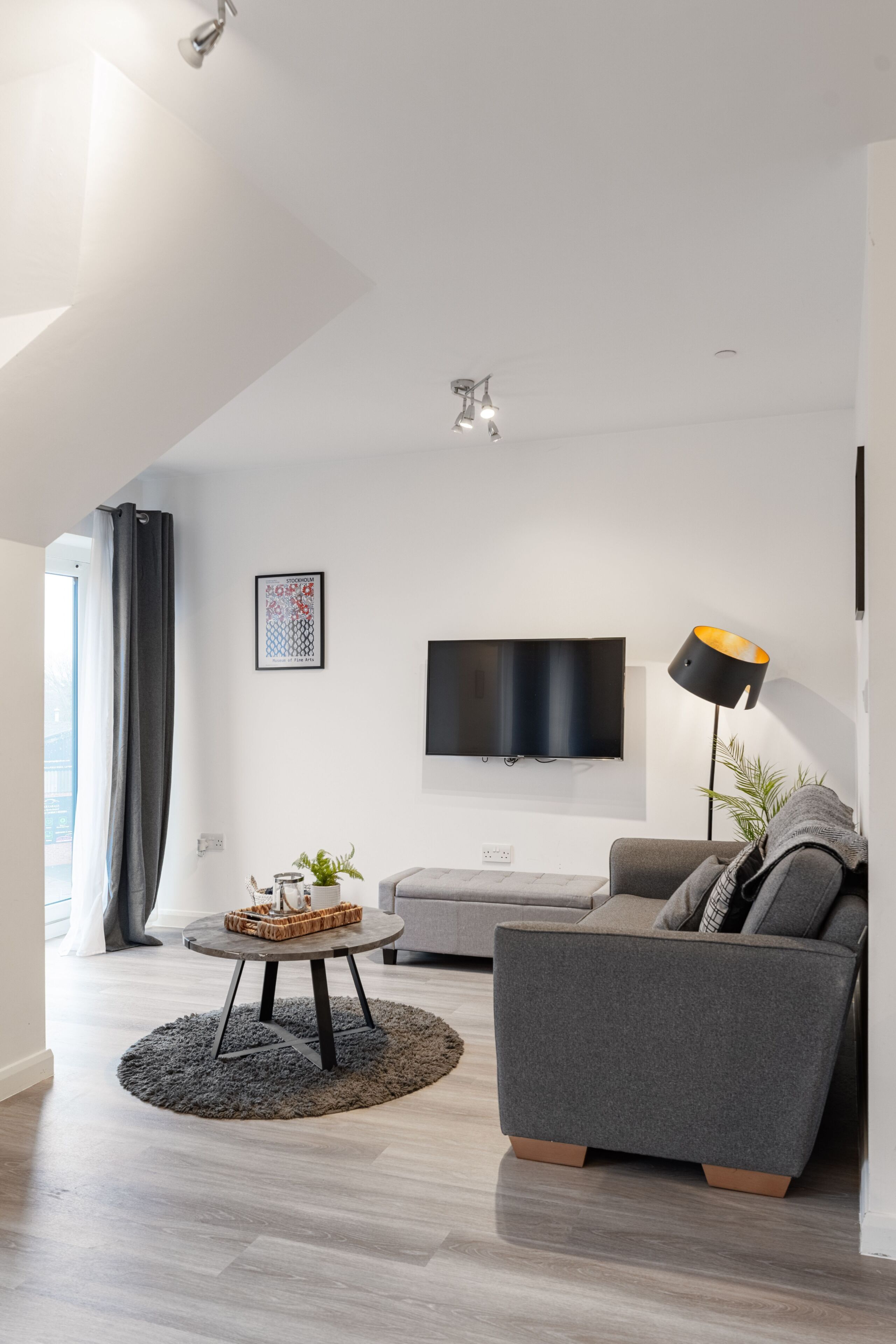 A modern living room with a grey sofa, a round coffee table, and a flat-screen TV mounted on the wall.