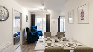 Un coin repas avec une table dressée pour quatre personnes, un fauteuil bleu et une vue par la fenêtre.