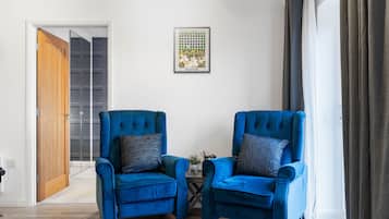 A room with two blue armchairs, a small table, a framed picture on the wall, and a door leading to another room.