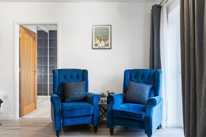A room with two blue armchairs, a small table, a framed picture on the wall, and a door leading to another room. - Aura Retreat- 1 Bedroom Apartment (York)